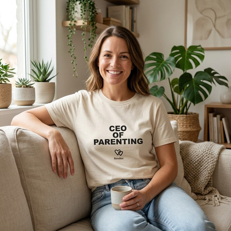 Smiling woman in a cream Bondkin CEO of Parenting tee on a sofa with a coffee cup