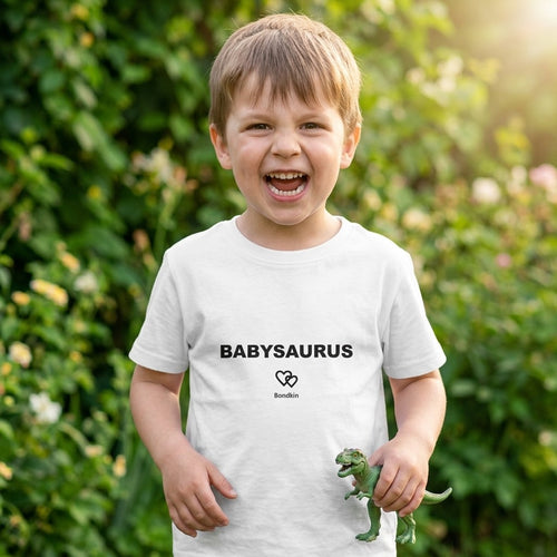 Laughing boy in a white Bondkin Babysaurus tee holding a toy dinosaur